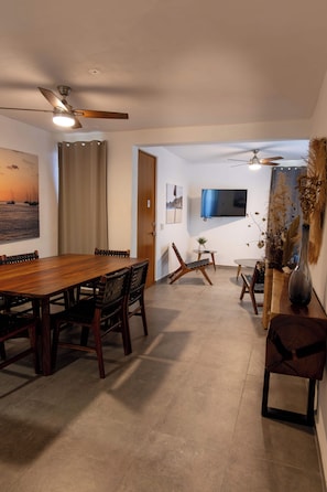 A dining area with a wooden table and chairs, a ceiling fan, and a television mounted on the wall. - Departamento San Luisito (Puerto Vallarta)