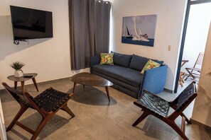 Ein Wohnzimmer mit einer Couch, zwei Sesseln, einem Couchtisch, einem Fernseher, einem Gemälde und einer kleinen Pflanze.