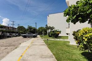 A paved sidewalk adjacent to a building with a grassy area and parked vehicles. - Departamento San Luisito (Puerto Vallarta)