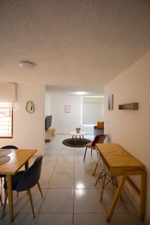 A modern living room with a dining area, a TV, and a sofa. - Departamentos Las Rosas Expo GDL (Guadalajara)