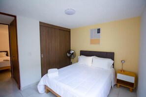 Ein Hotelzimmer mit Bett, Nachttisch, Ventilator und Kleiderschrank.