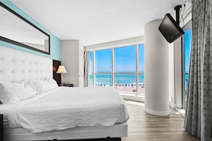 Une chambre d  ’hôtel dotée d’un grand lit, d’un téléviseur à écran plat fixé au mur et offrant une vue sur la plage grâce à de grandes fenêtres.