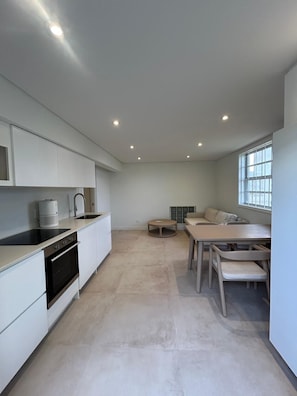 Ett modernt kök med vita köksskåp, en svart spis och ett runt matbord med stolar.