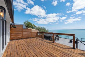 A wooden deck with a railing, overlooking a body of water and a clear sky.