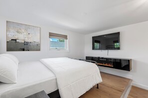 A modern bedroom with a bed, a fireplace, a television, and artwork on the wall.