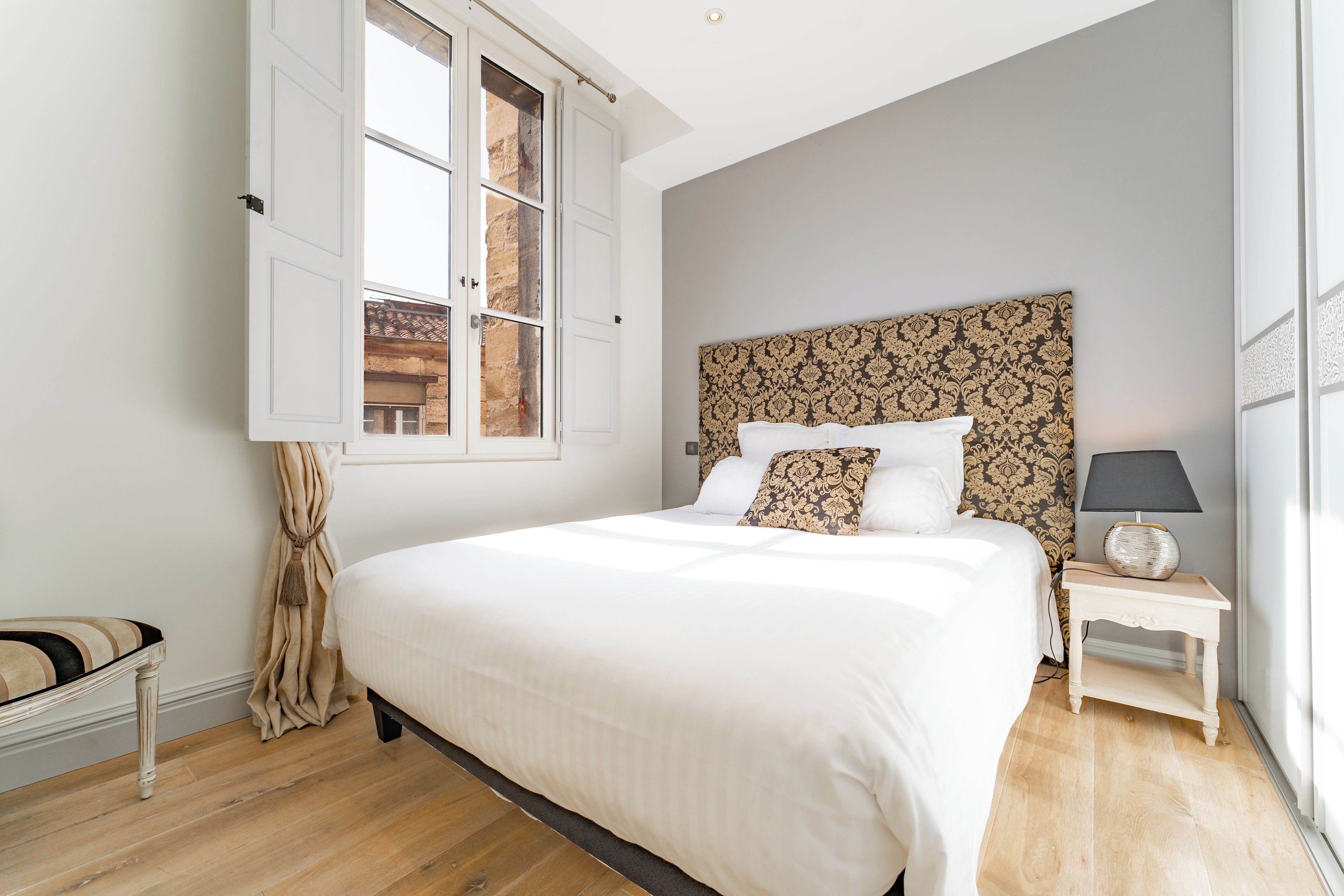 A bedroom with a large bed, a nightstand, a lamp, and a window with curtains.