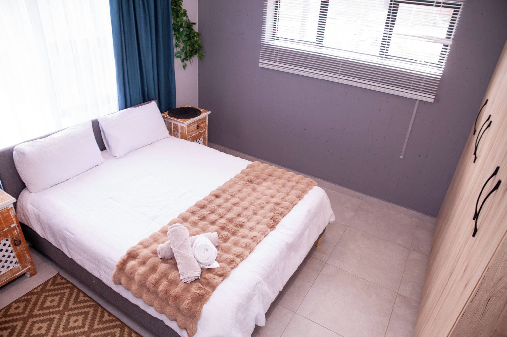 Una cama bien hecha con sábanas blancas, un edredón beige suave y una toalla enrollada en el reposapiés.