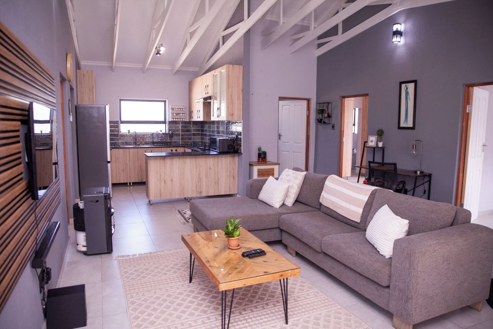 A modern living room with a grey sofa, a wooden coffee table, and a kitchen in the background.