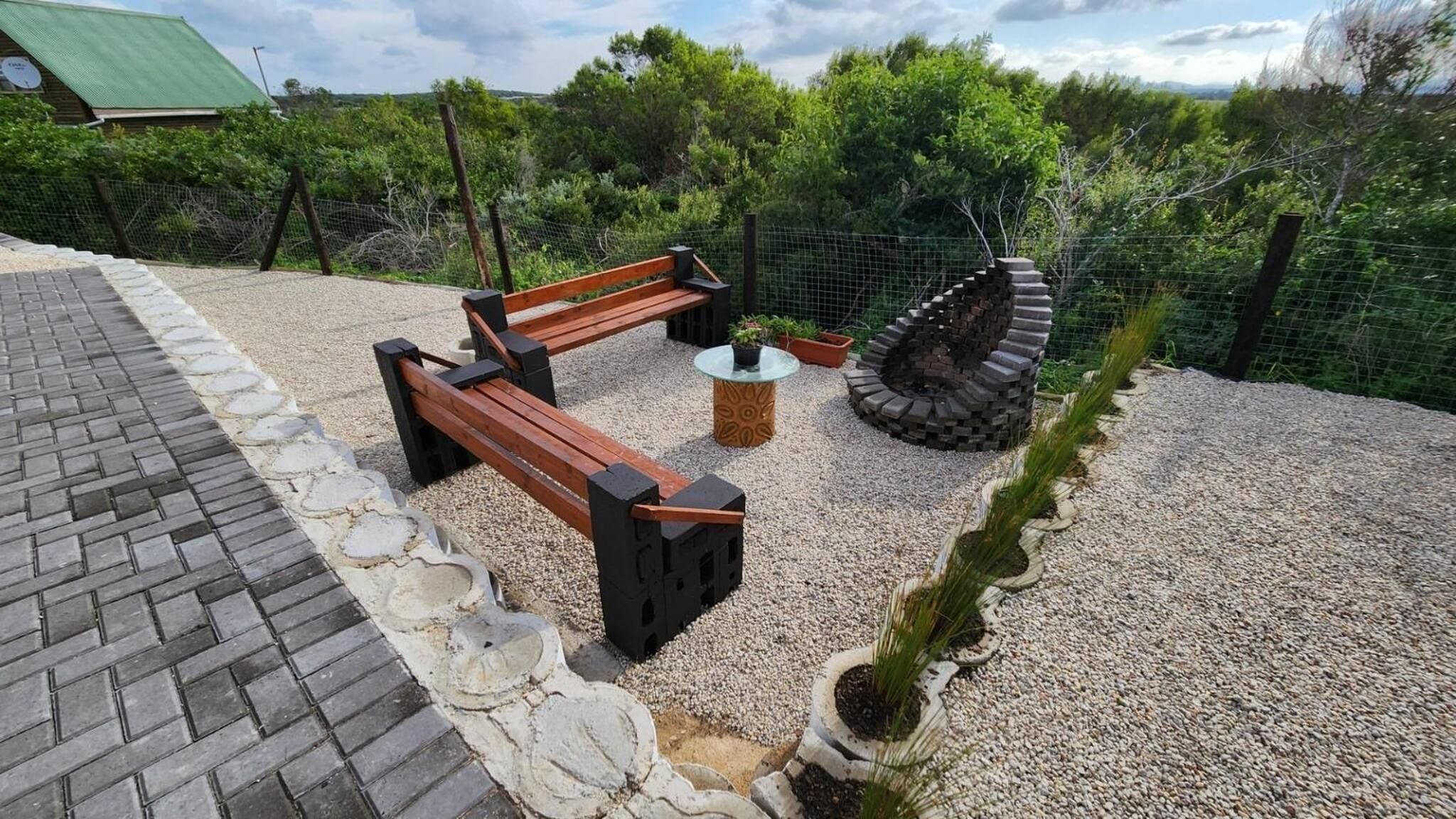 Un espacio al aire libre con asientos, una banca, una mesa redonda y un original hogar de piedra.