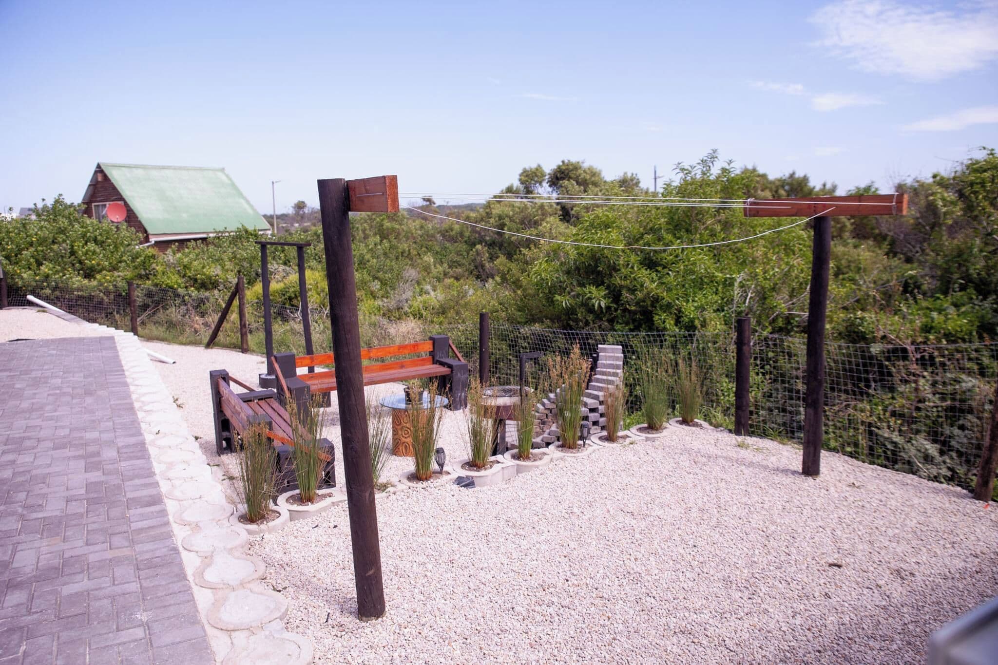 A gravel patio with a wooden bench and a pergola structure.