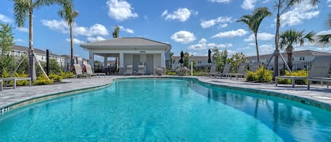 A clear blue swimming pool with lounge chairs and palm trees.
