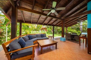 A covered outdoor seating area with a wooden ceiling, a sofa, a table, and a grill. - Pool ~ BBQ ~ Walk to Beach ~ Golf Cart Parking ~ 3 TVs - Villaggio 324 (Potrero)