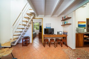 A spacious living area with a wooden staircase, a dining table with stools, a flat-screen TV, and a bookshelf. - Pool ~ BBQ ~ Walk to Beach ~ Golf Cart Parking ~ 3 TVs - Villaggio 324 (Potrero)