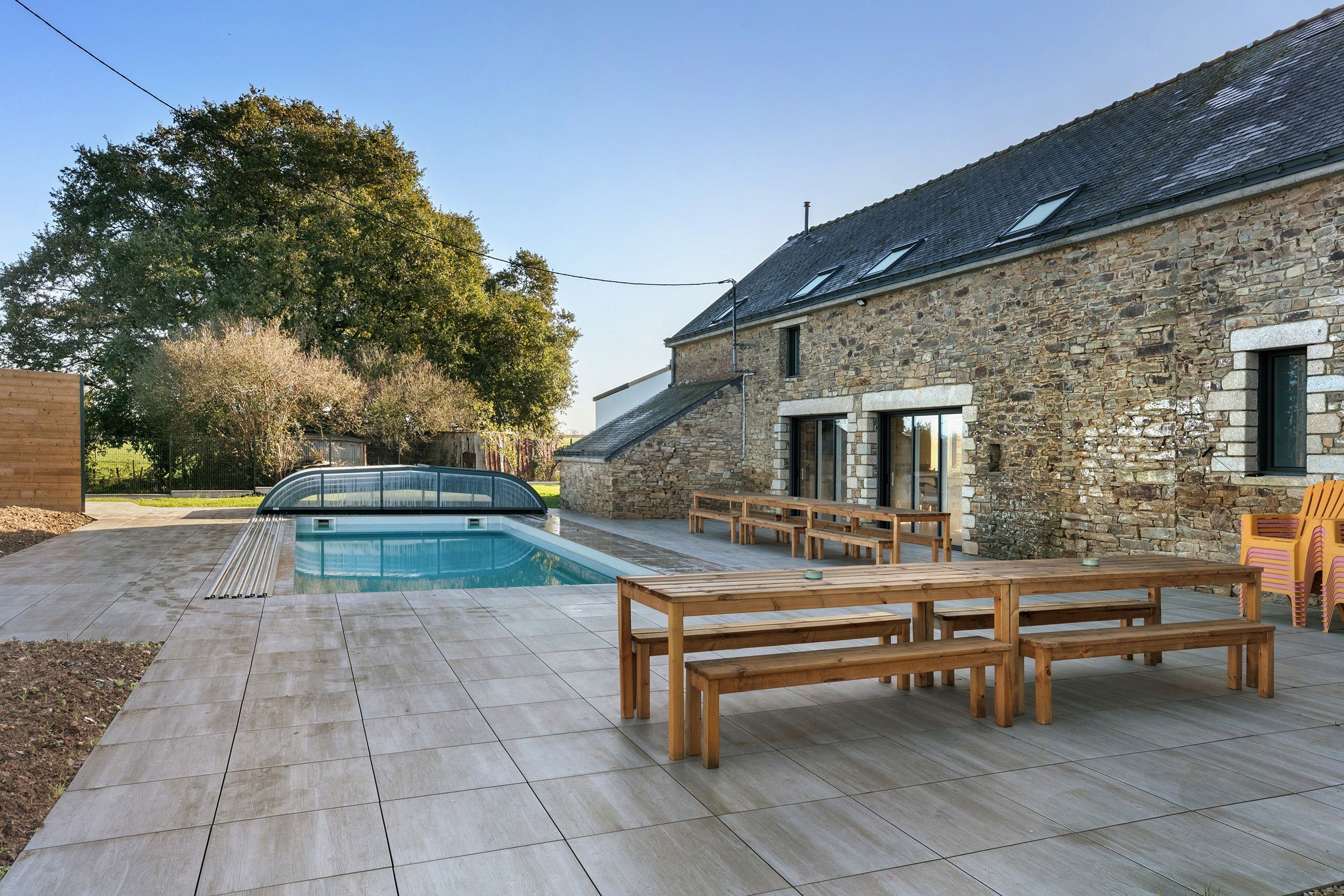 A stone building with a swimming pool, wooden benches, and a covered area.