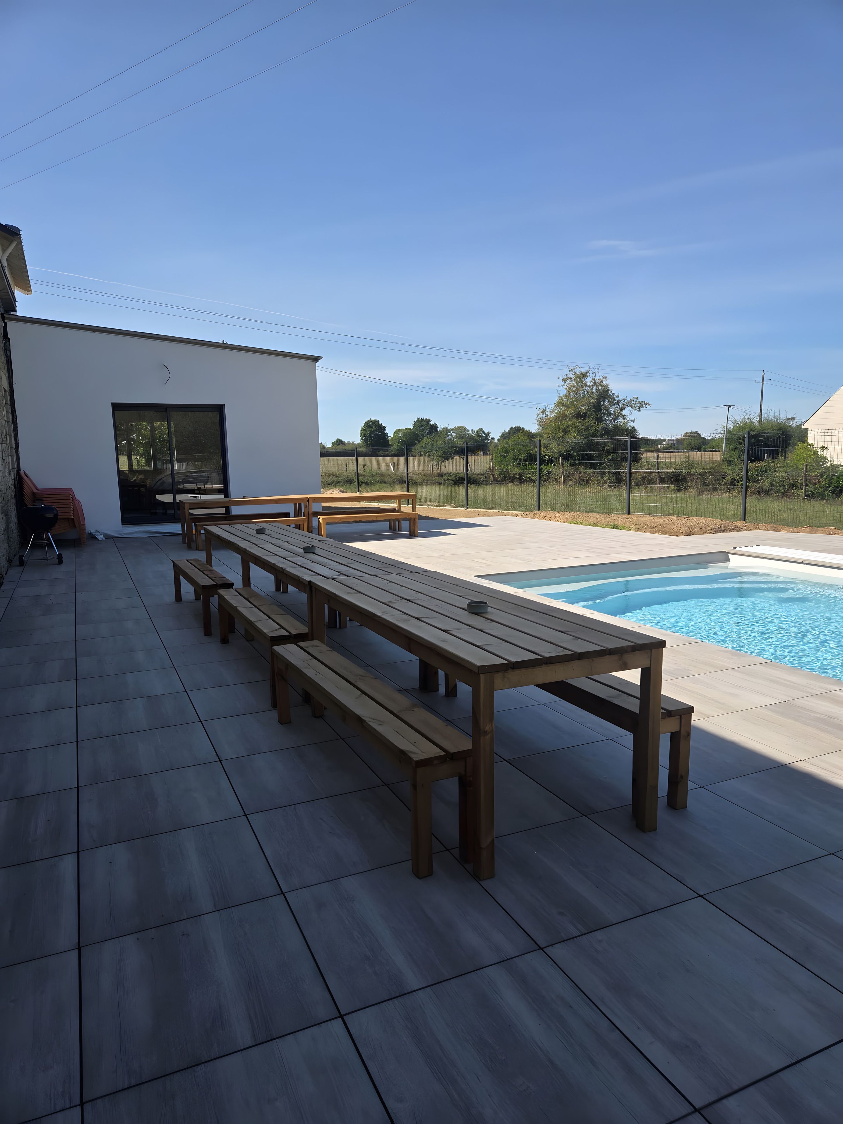 A poolside area with a long wooden bench, a small table, and a covered seating area.