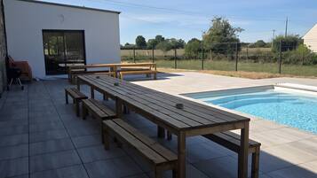 A poolside area with a long wooden bench, a small table, and a covered seating area.