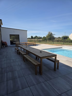 A poolside area with a long wooden bench, a small table, and a covered seating area. - Holiday Home 'Le Boizeul' with Private Pool, Terrace and Air Conditioning (Nivillac)