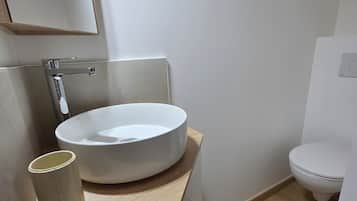 Un baño moderno con un lavabo redondo, un inodoro y un espejo.