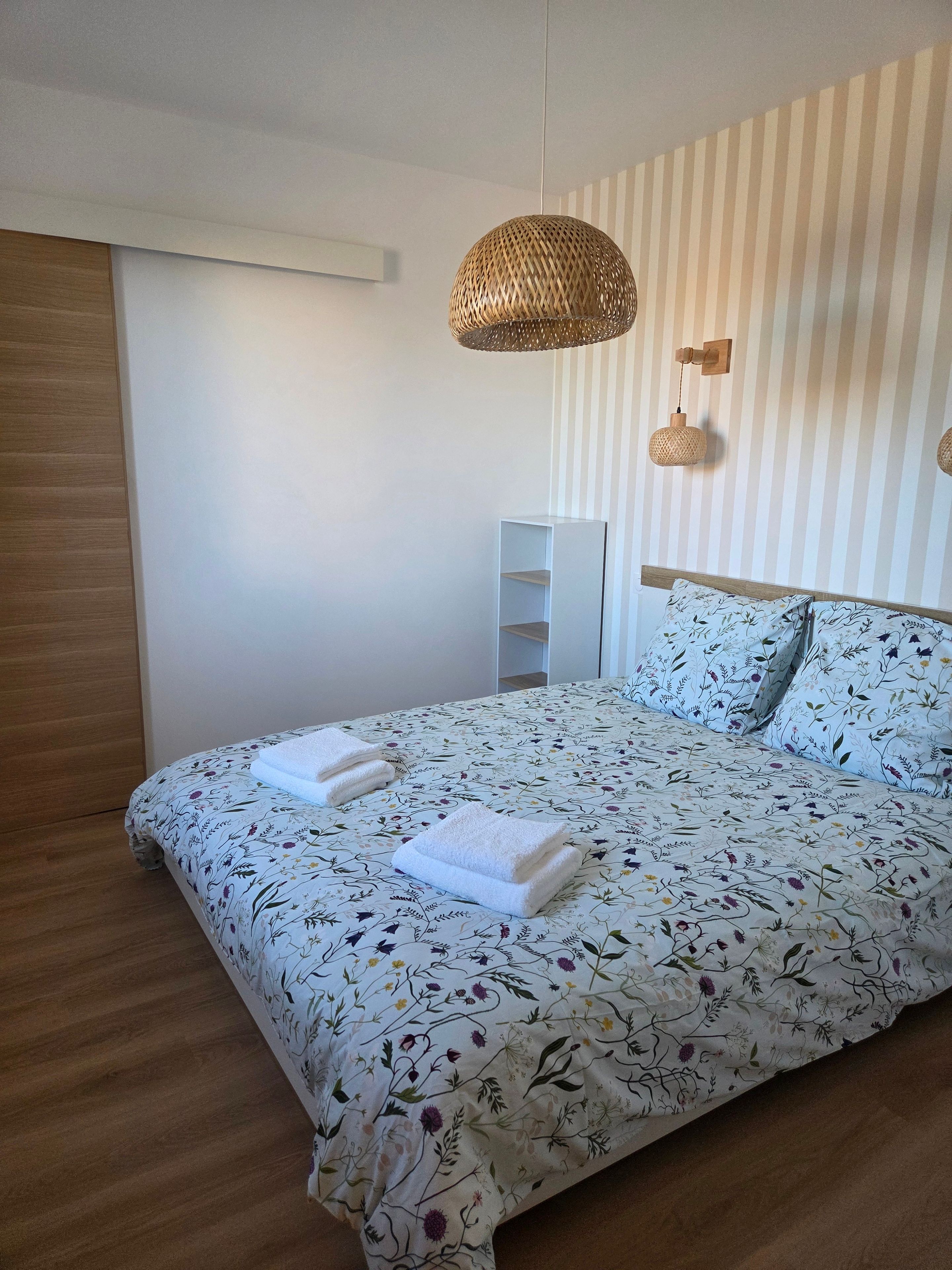 A bedroom with a bed, two bedside tables, a hanging light fixture, and a striped wall.