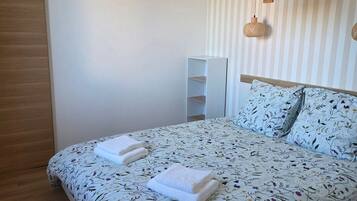 A bedroom with a bed, two bedside tables, a hanging light fixture, and a striped wall.