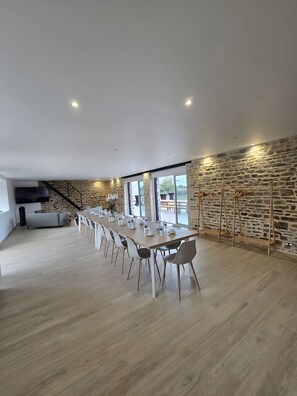Un vaste espace dédié à la salle à manger, avec une longue table, des chaises et un mur en pierre.