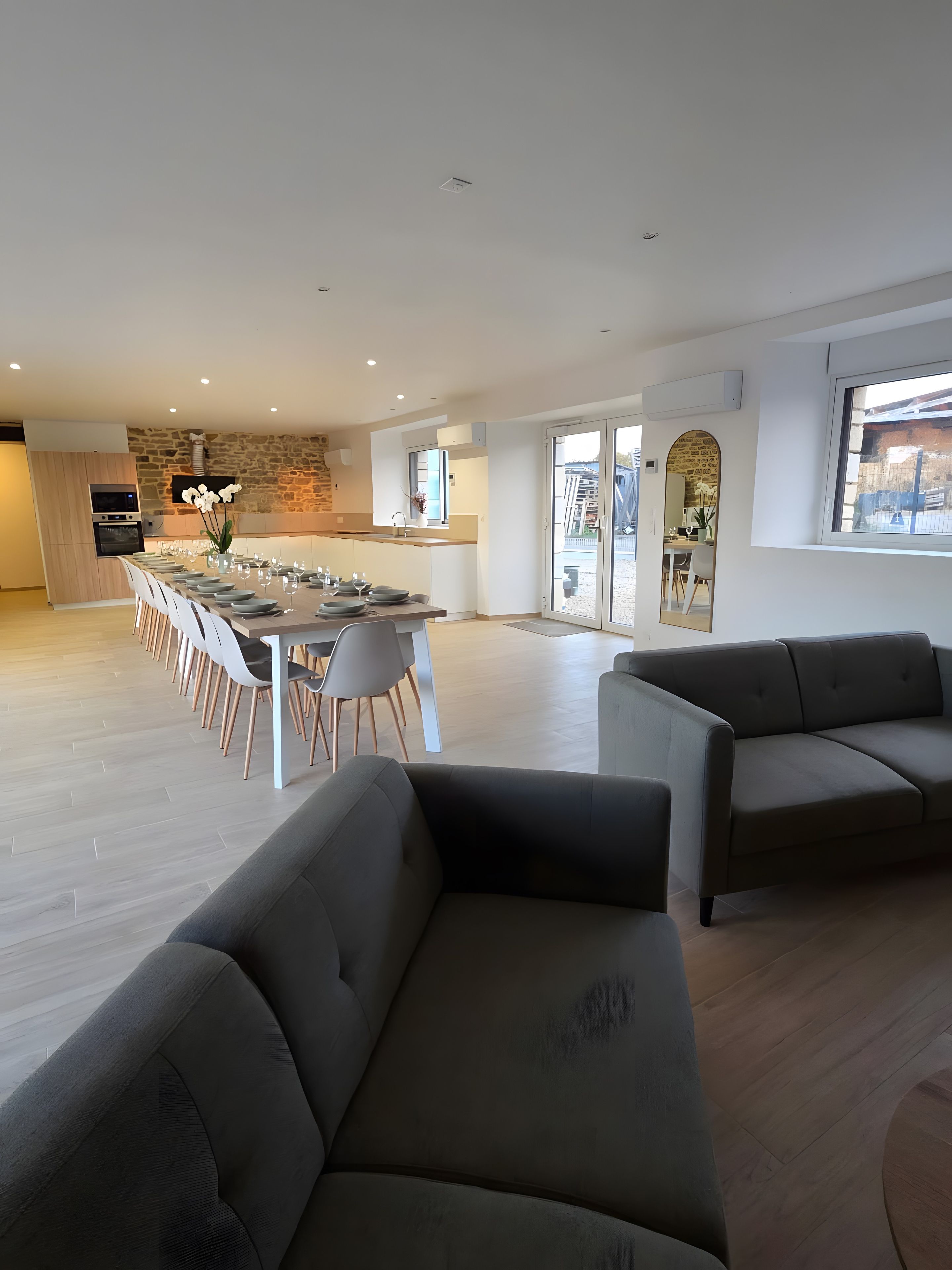 A spacious living area with a dining table set for six, a sofa, and a kitchen in the background.