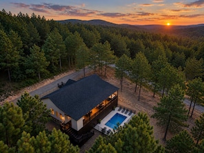 Ein modernes, zweistöckiges Haus mit Pool, eingebettet in eine bewaldete Landschaft, während der Sonnenuntergang beginnt.