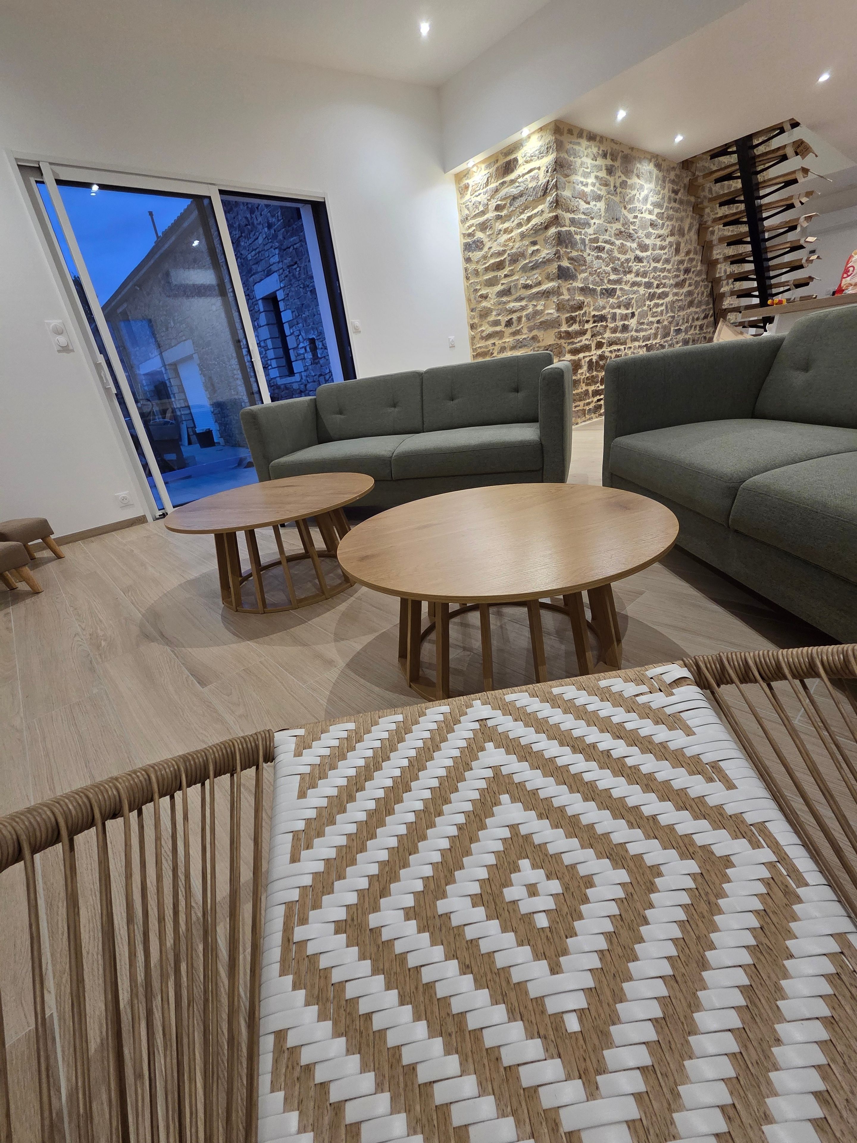 A modern living room with a stone accent wall, a grey sofa, two round wooden tables, and a patterned rug.