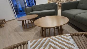 A modern living room with a stone accent wall, a grey sofa, two round wooden tables, and a patterned rug.