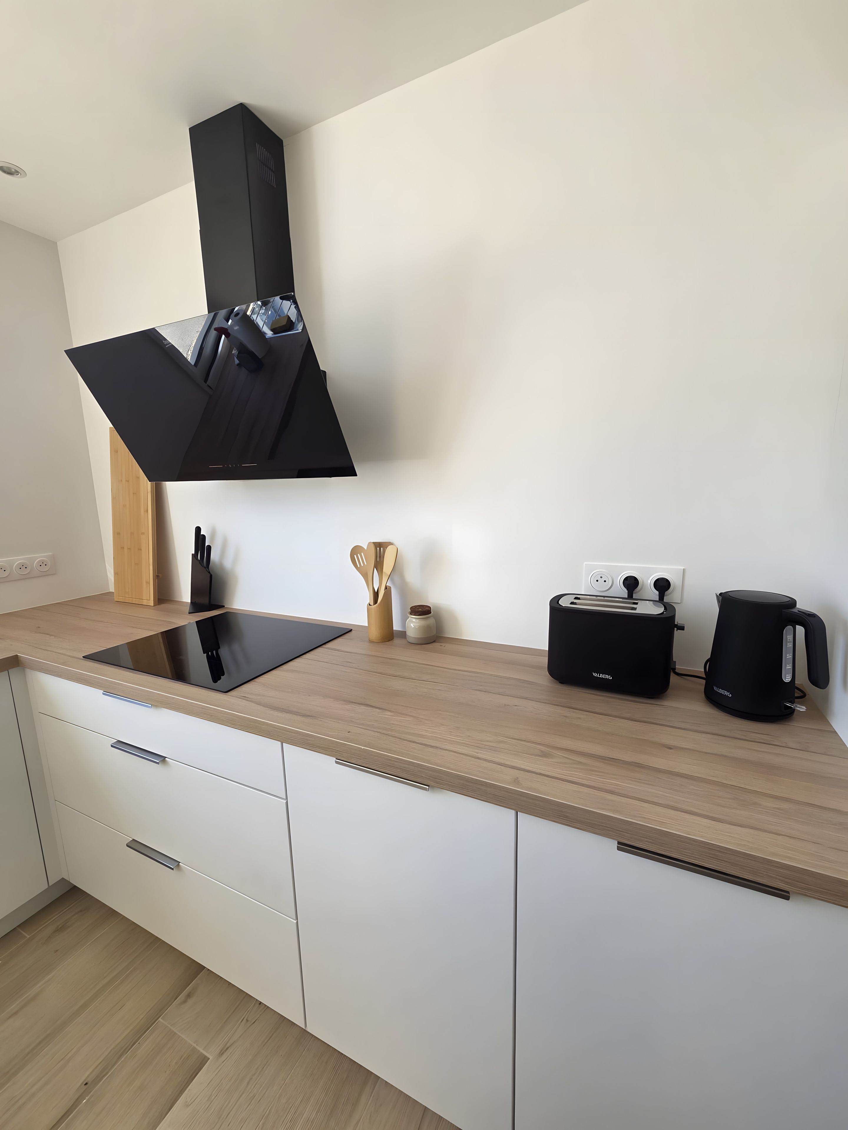 Une cuisine moderne avec une plaque de cuisson à induction noire, un grille-pain et une machine à café, le tout posé sur un plan de travail en bois.