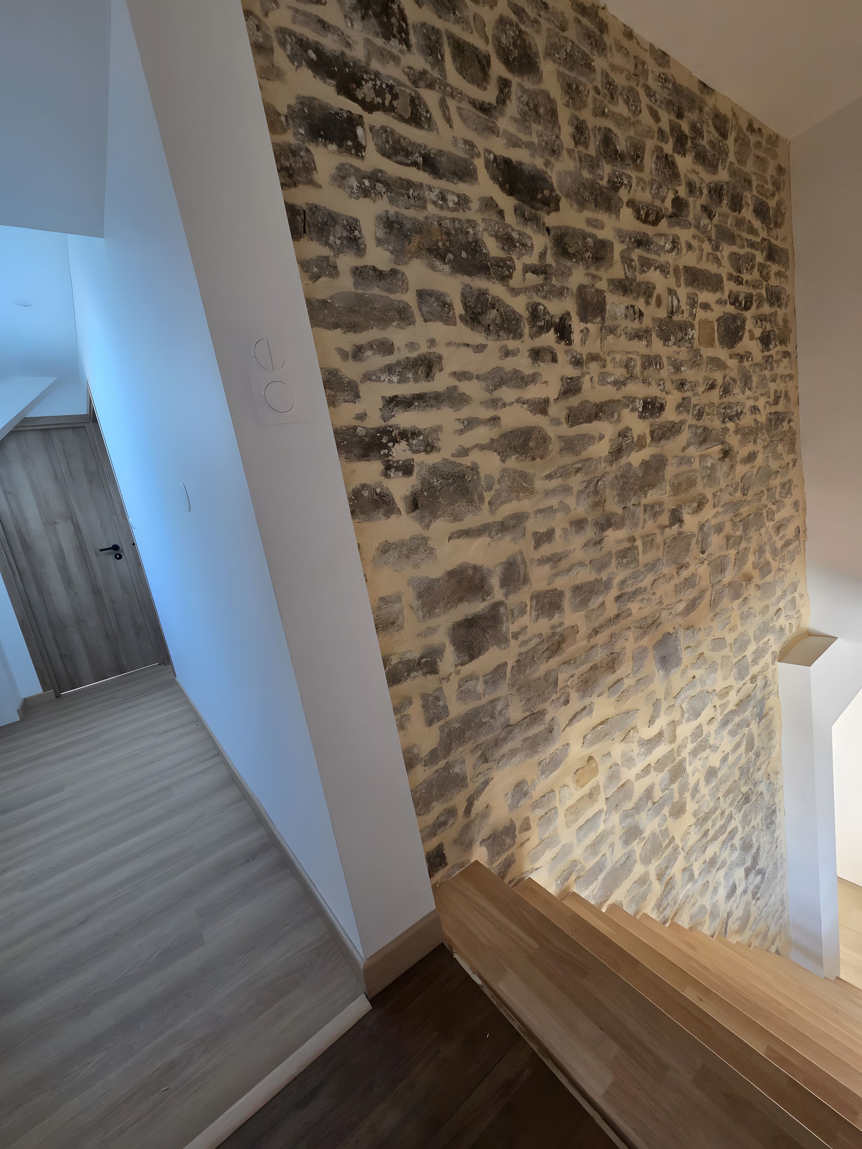 Quarto com parede de pedra, piso de madeira e porta branca.