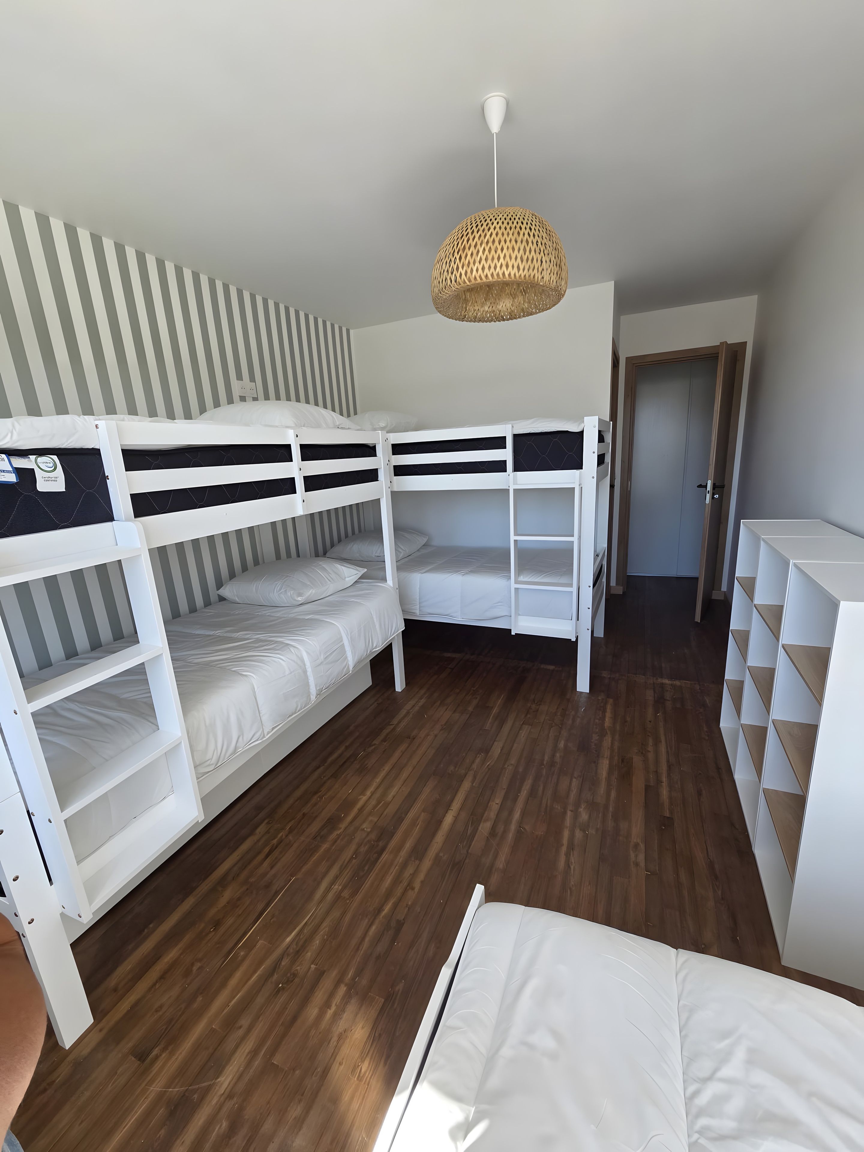 A bunk bed room with a wooden floor, a striped wall, and a hanging light fixture.