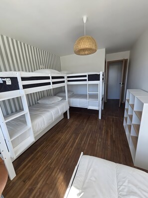 Een slaapkamer met stapelbed, houten vloer, een gestreepte wand en een hanglamp.