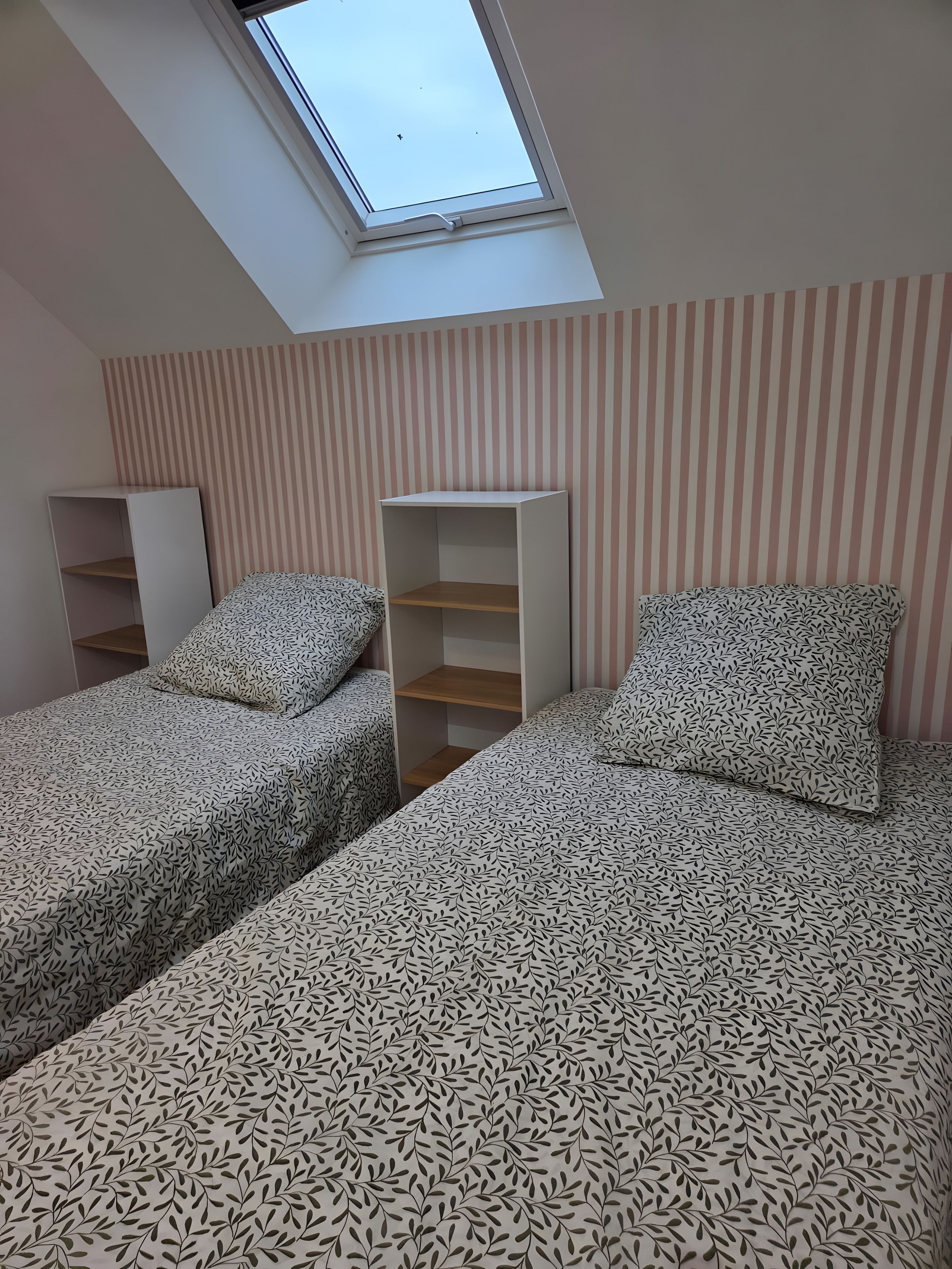 Quarto com duas camas, um claraboia, parede listrada e um armário branco.