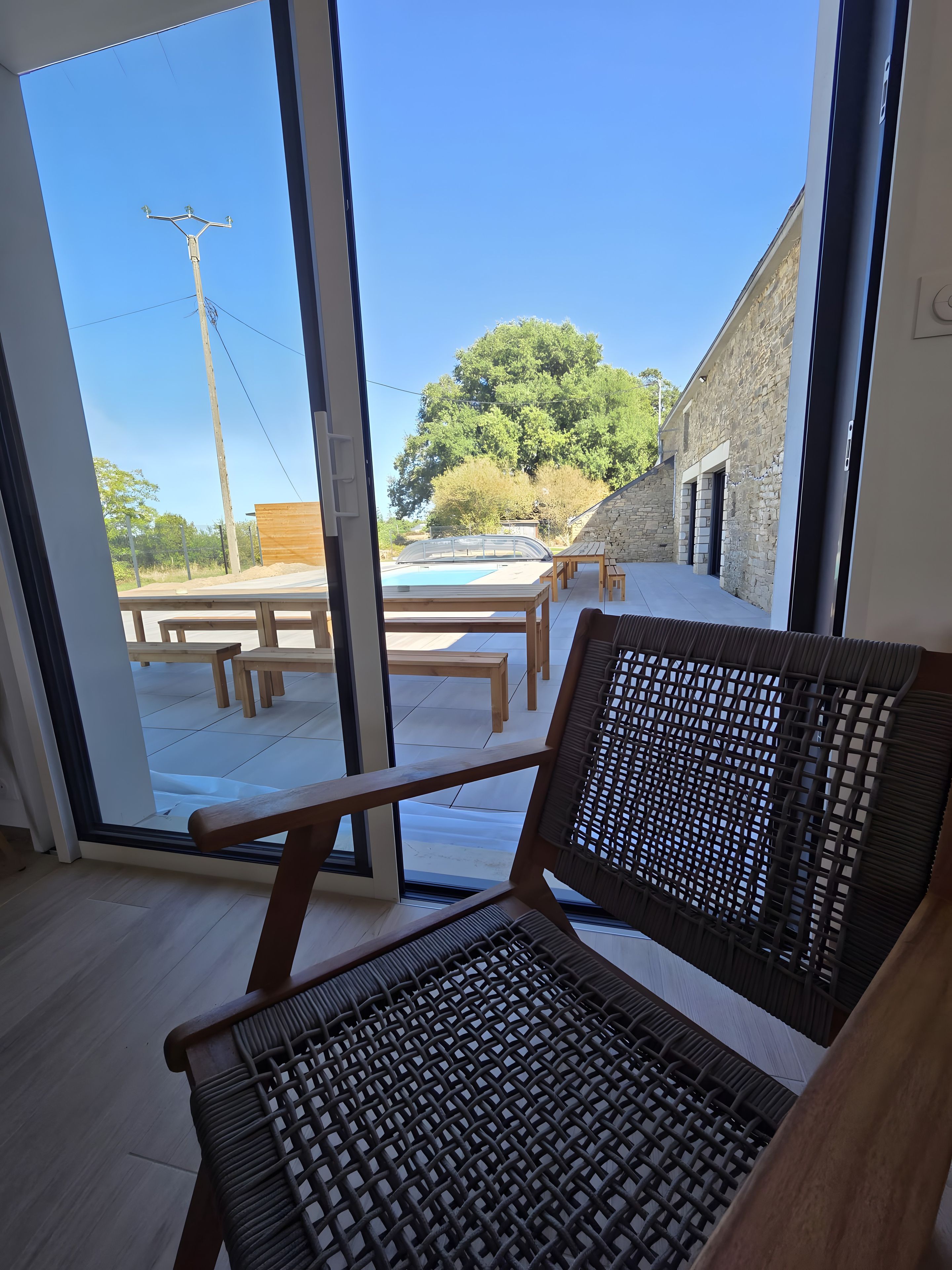 A room with a view of an outdoor swimming pool, wooden benches, and a stone building.