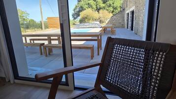 A room with a view of an outdoor swimming pool, wooden benches, and a stone building.