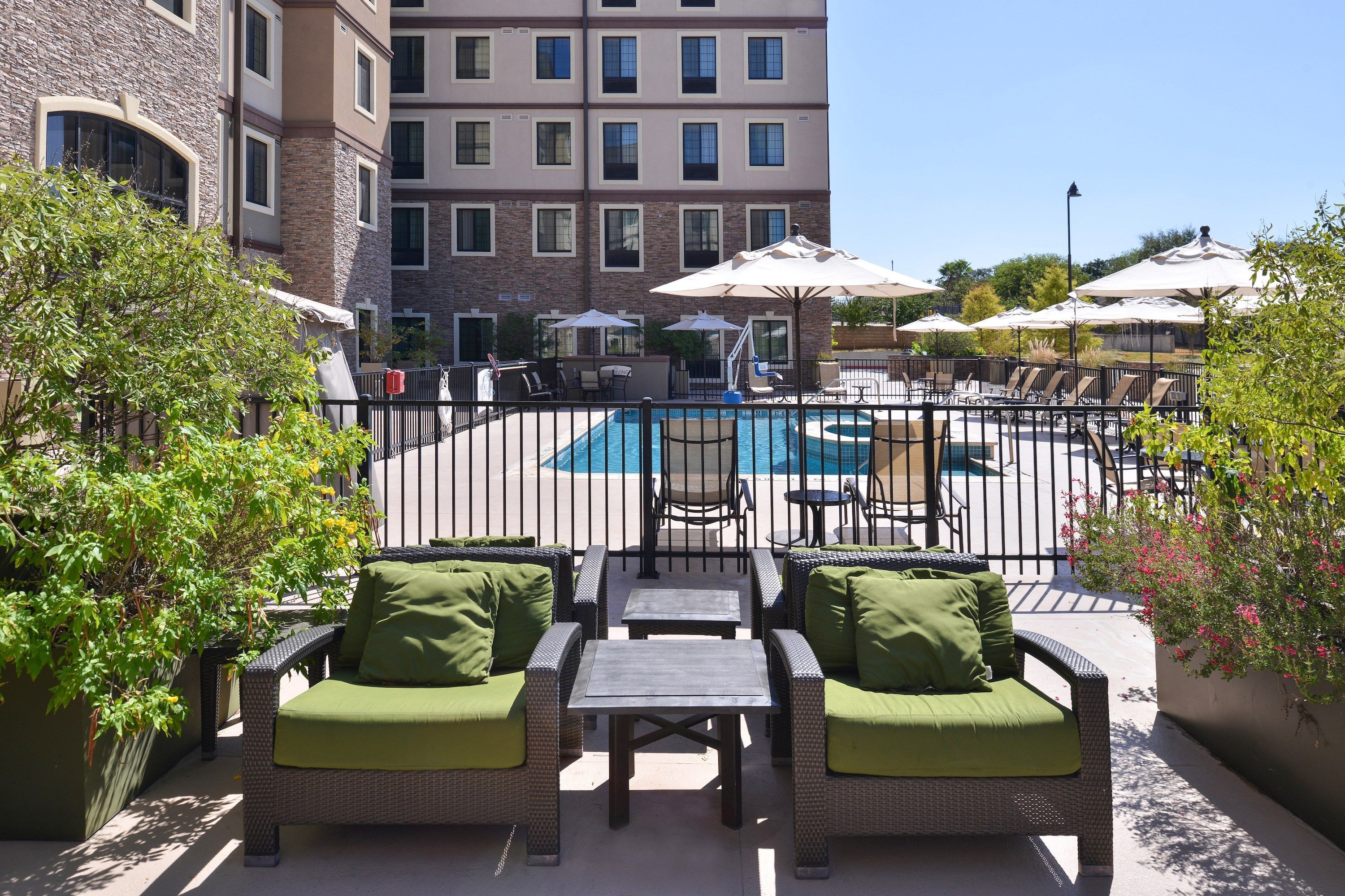 A poolside area with wicker furniture, umbrellas, and a view of a building in the background.