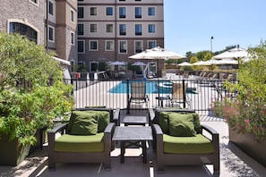 A poolside area with wicker furniture, umbrellas, and a view of a building in the background. - King Studio w/ Kitchen | Daily Breakfast + Pool (San Antonio)