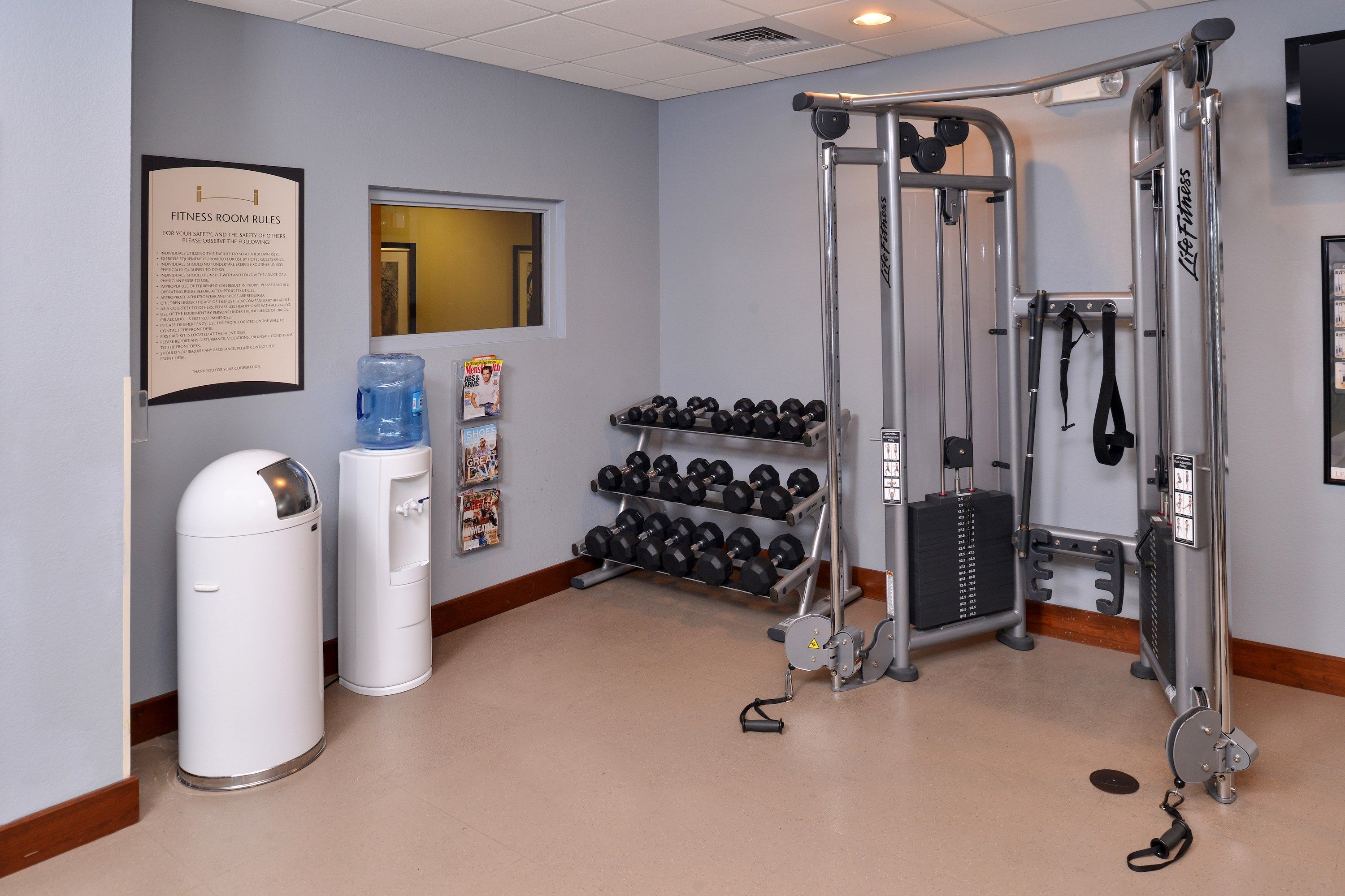 A fitness room with exercise equipment, a water dispenser, and a wall-mounted sign with rules.