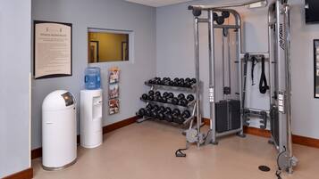 A fitness room with exercise equipment, a water dispenser, and a wall-mounted sign with rules.