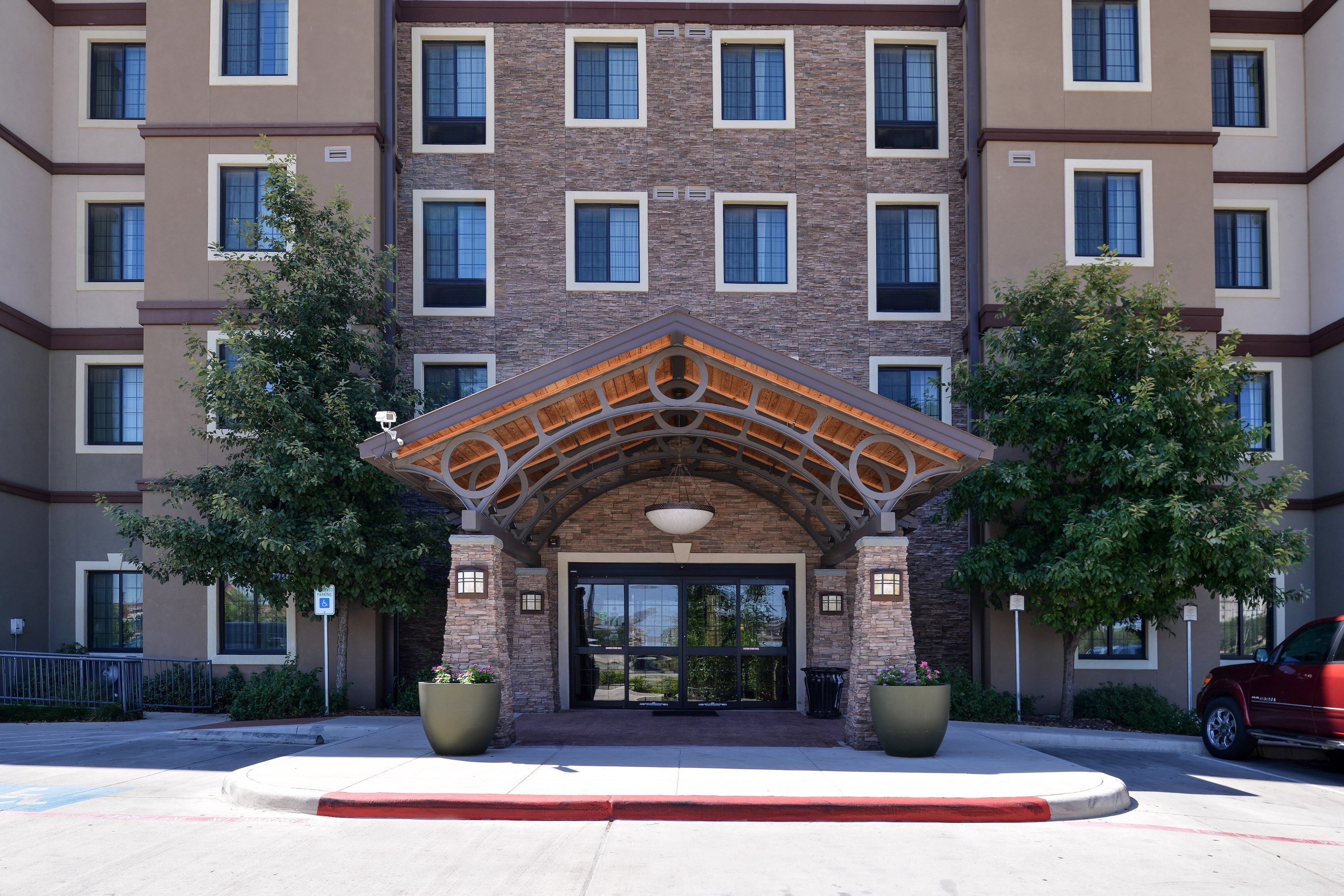 A multi-story building with a central entrance featuring a wooden archway and large potted plants on either side.