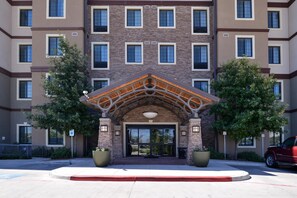 A multi-story building with a central entrance featuring a wooden archway and large potted plants on either side. - 2 Double Studio w/ Kitchen & Free Daily Breakfast (San Antonio)