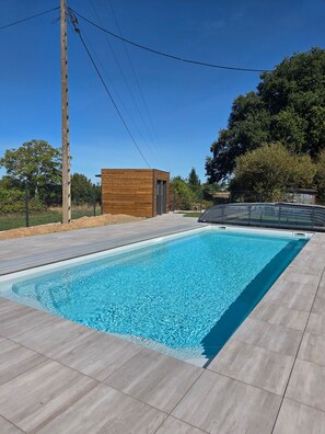 A swimming pool with a wooden deck and a small building in the background. - Group Cottages Les Boizeul Pool - 2x15 Guests with Private Pool, Air Conditioning and Wi-Fi (Nivillac)