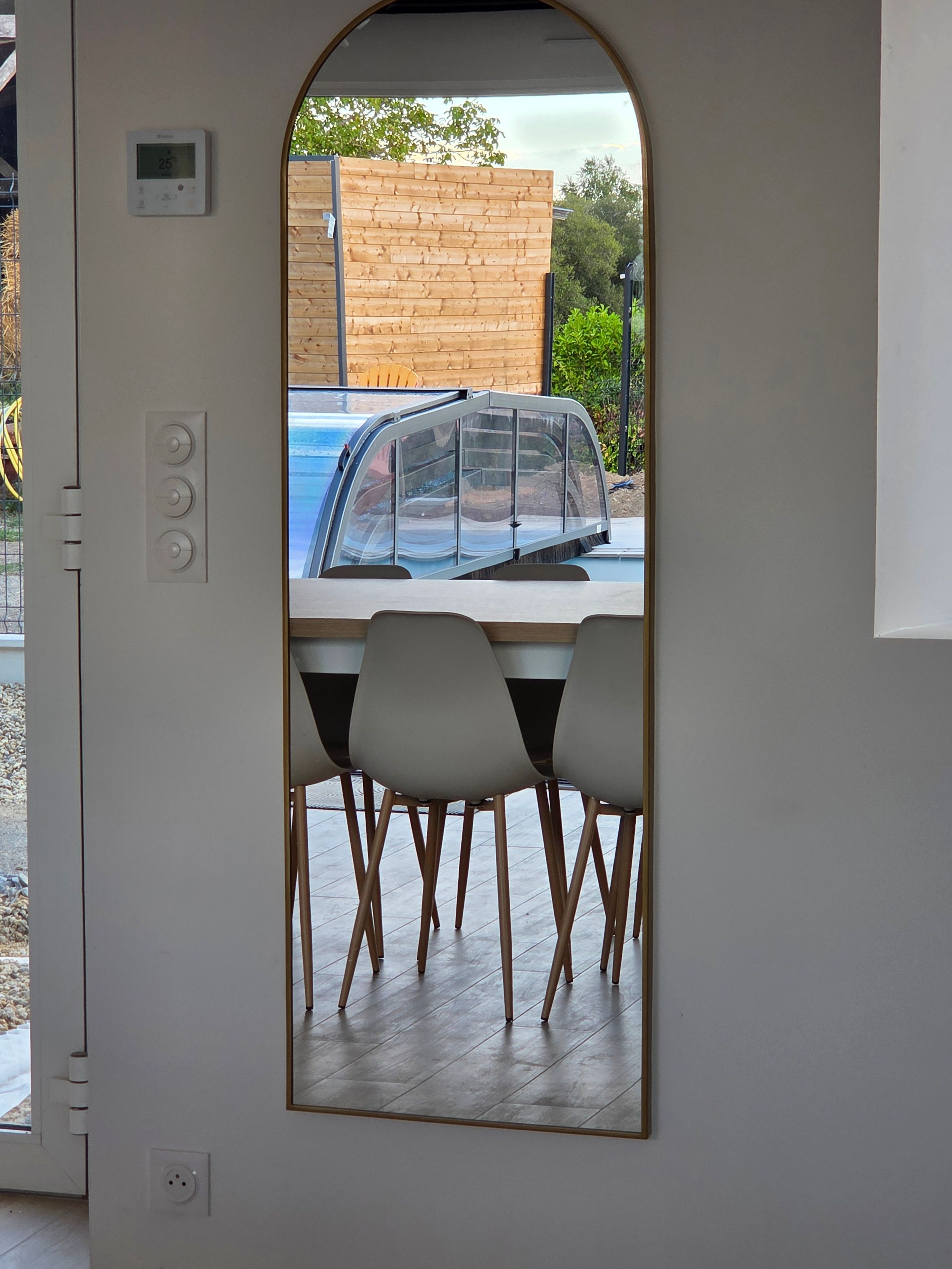 A view through a door of a dining area with a table and chairs, a car parked outside, and a wooden fence in the background.