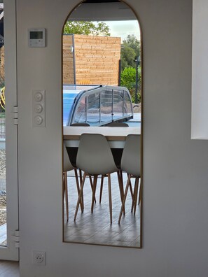 A view through a door of a dining area with a table and chairs, a car parked outside, and a wooden fence in the background. - Group Cottages Les Boizeul Pool - 2x15 Guests with Private Pool, Air Conditioning and Wi-Fi (Nivillac)