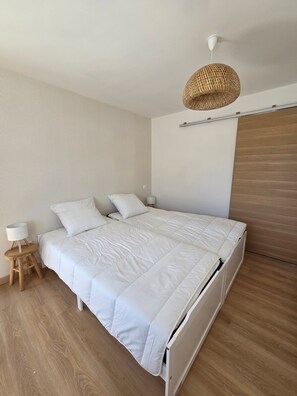 A neatly made bed with a white comforter and pillows, a bedside lamp on a wooden stool, and a woven pendant light fixture. - Group Cottages Les Boizeul Pool - 2x15 Guests with Private Pool, Air Conditioning and Wi-Fi (Nivillac)