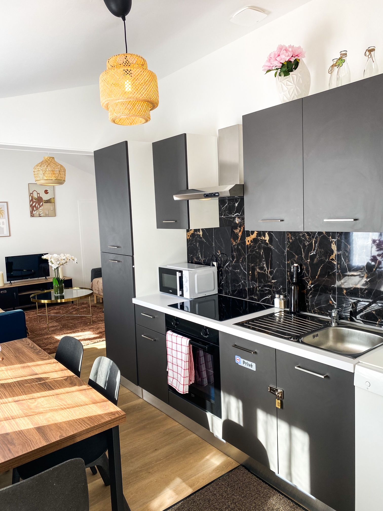 Una cocina moderna con microondas integrado, un lavamanos de acero inoxidable y una zona de comedor con mesa y sillas de madera.
