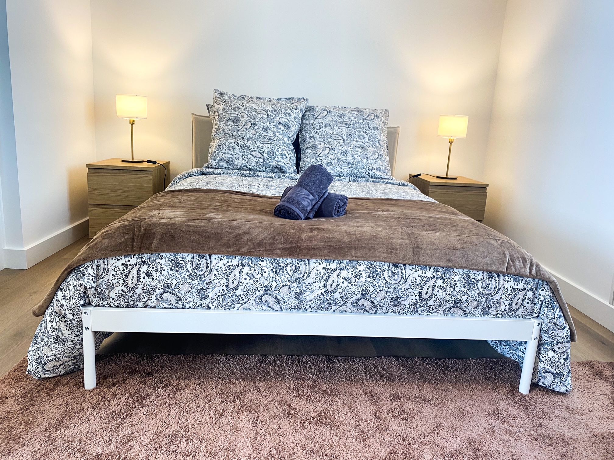 Un lit avec une couvre-lit à motifs et des oreillers, deux tables de chevet avec des lampes et un tapis marron.