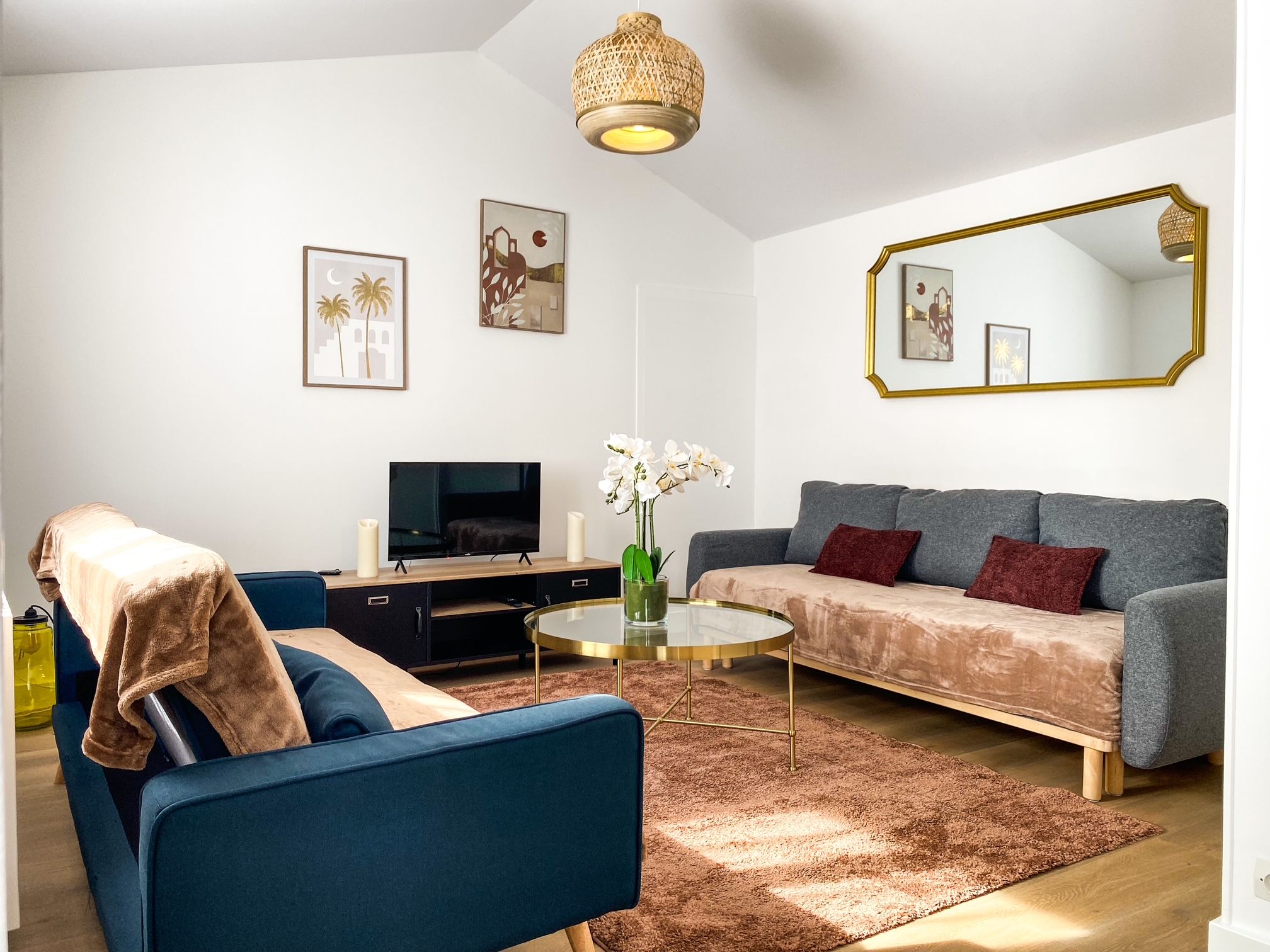 Un salon moderne avec un canapé bleu, un canapé gris, un téléviseur et un grand miroir.