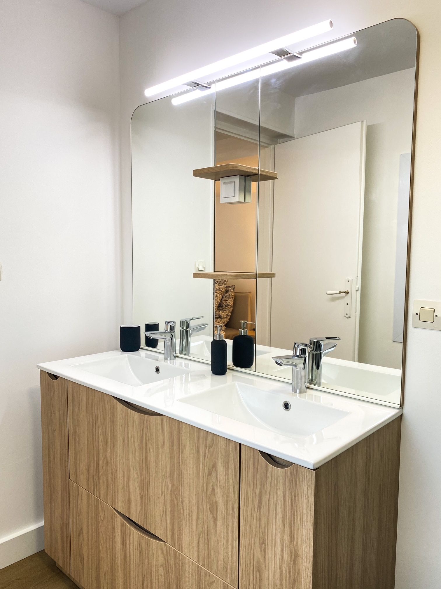 Un baño con tocador de doble lavabo, un espejo grande y una lámpara sobre el espejo.
